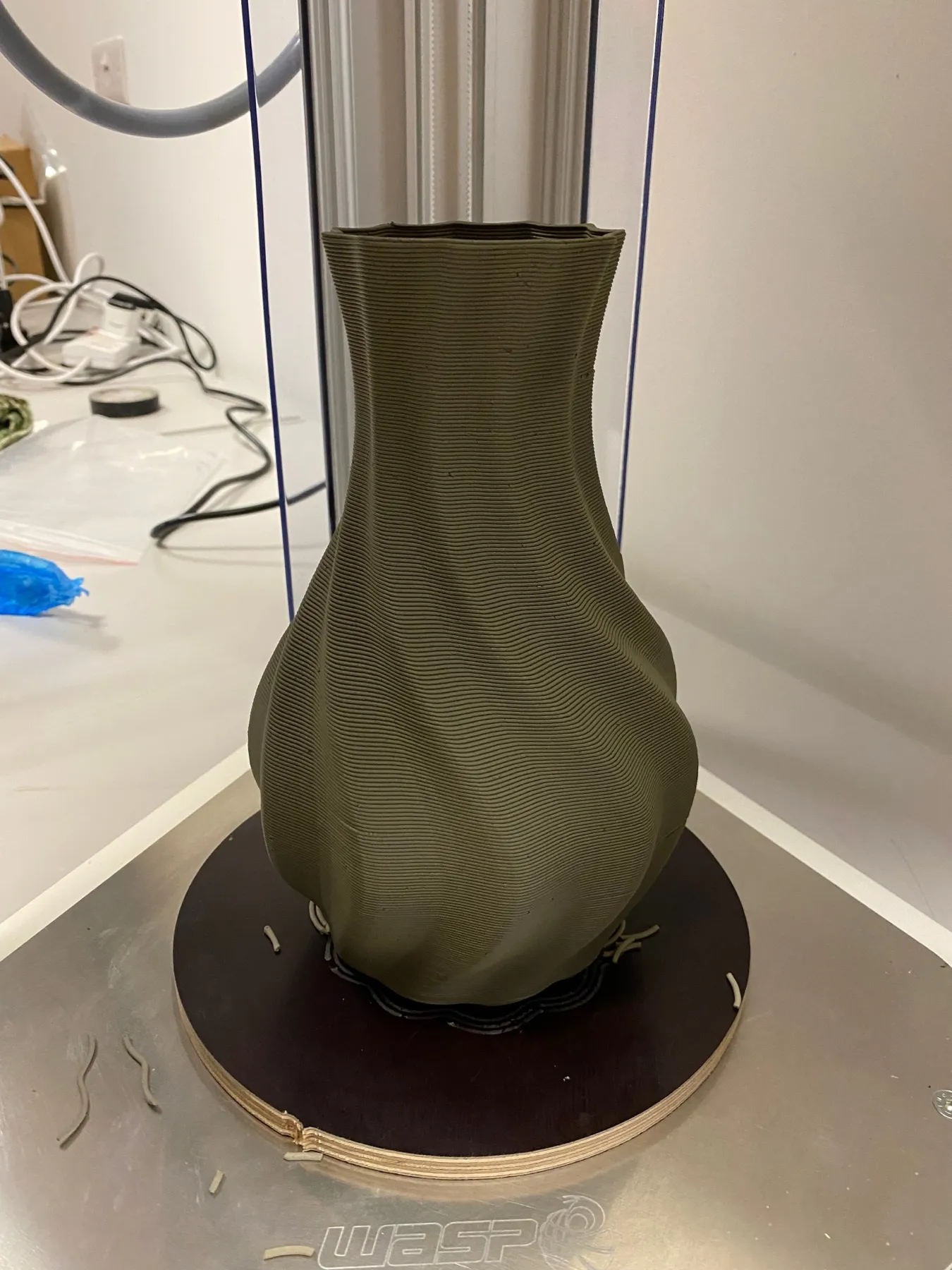 A clay printer with a freshly printed twisted vase, still wet, on its round bed