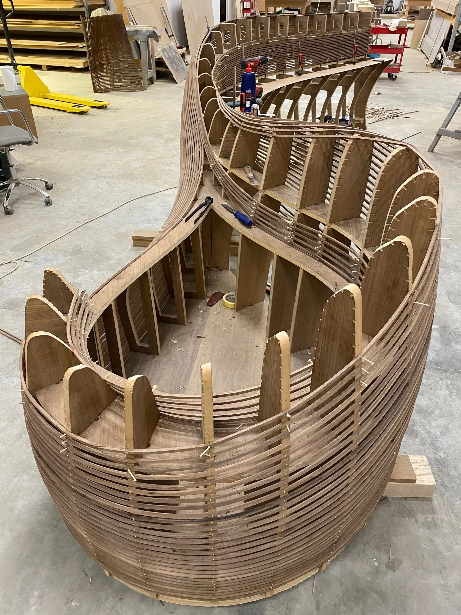 a long curved frame of timber ribs and strips being built on the factory floor