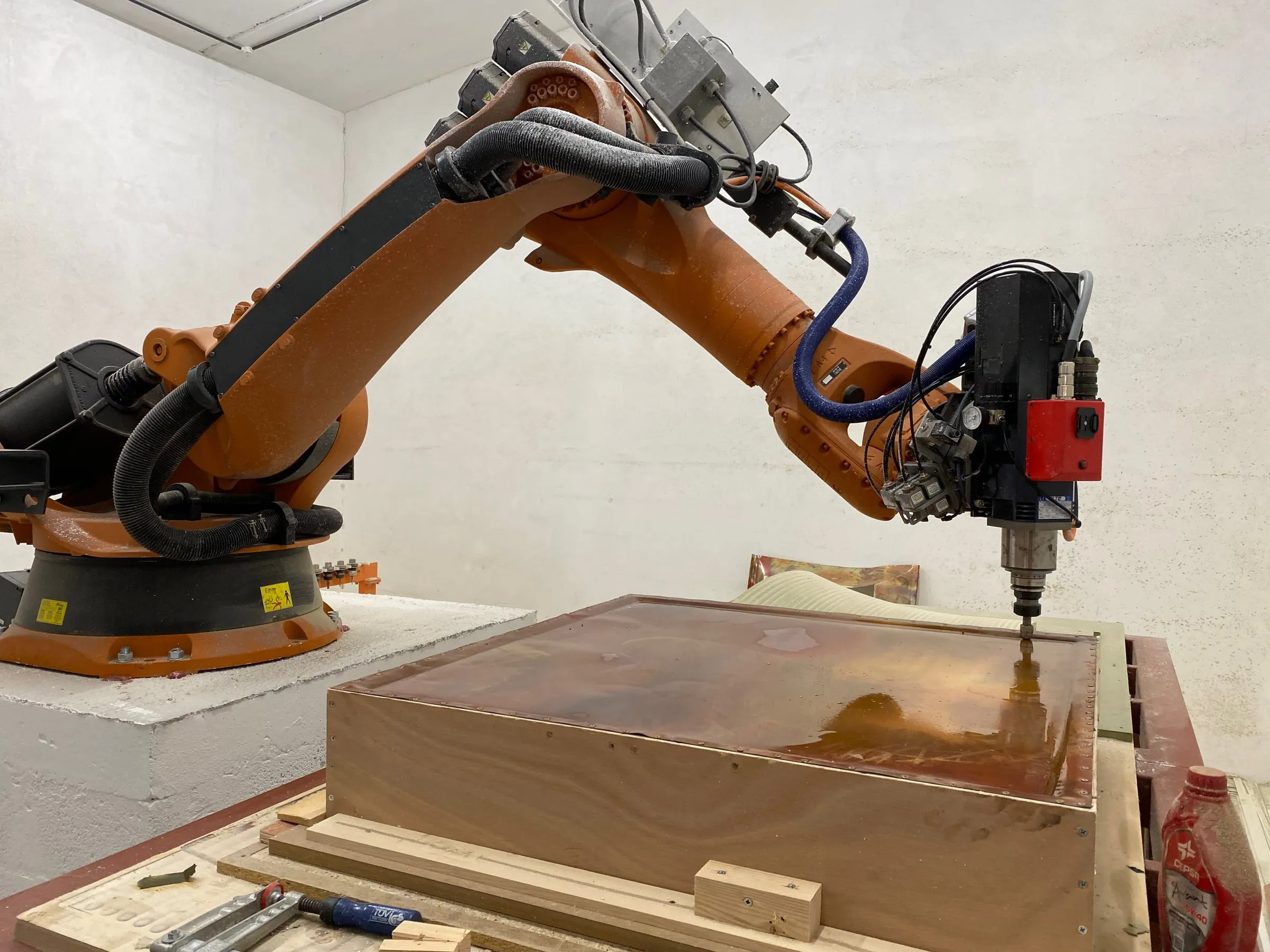 The robot arm pressing a copper sheet clamped in a timber frame