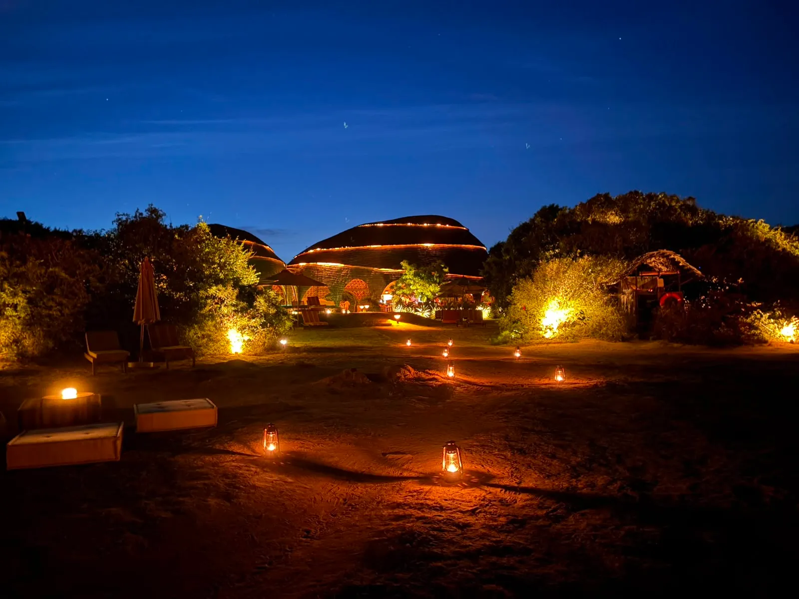lanterns glowing along a path at dusk, low buildings against a deep blue sky
