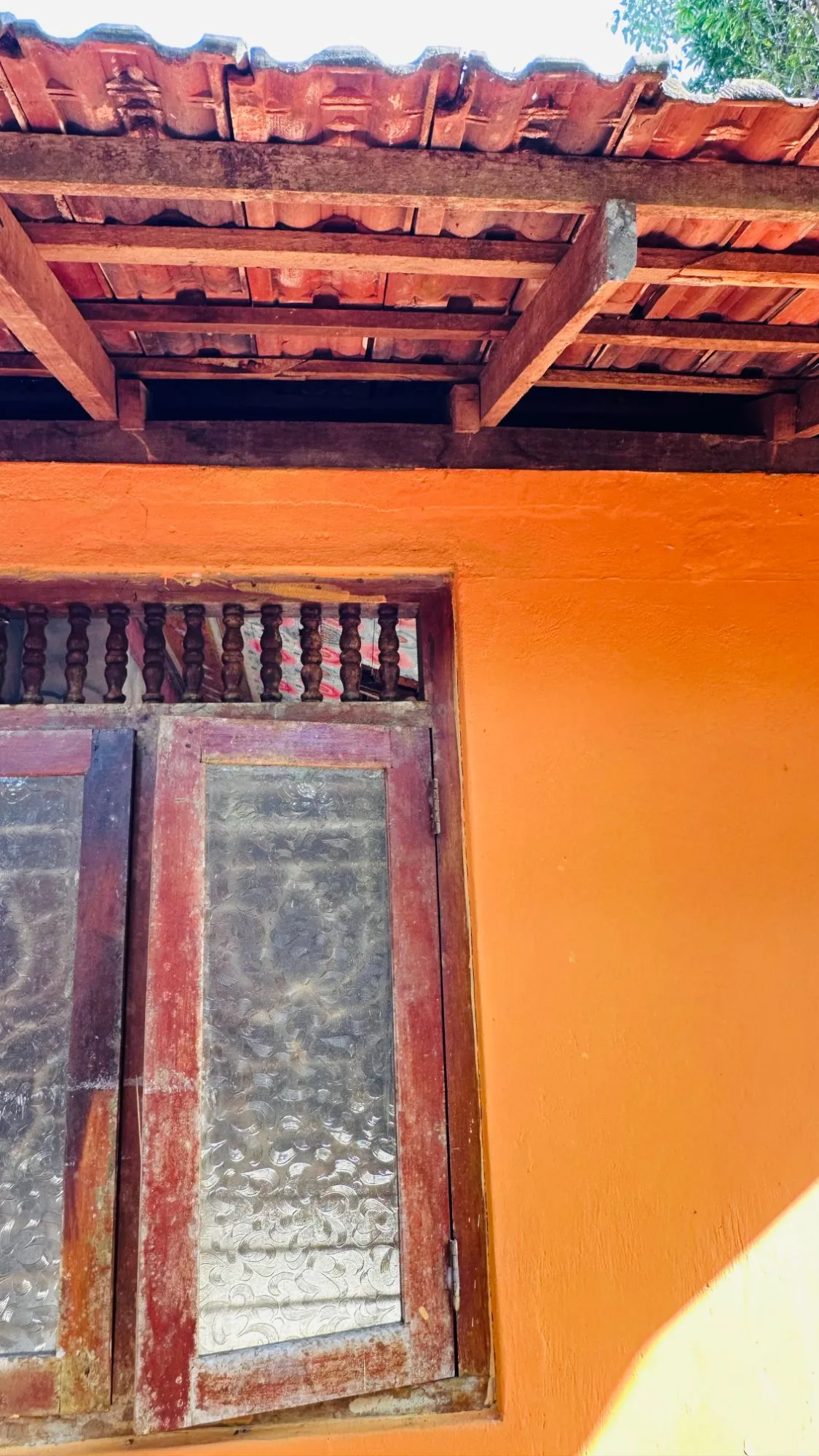 a timber window in an orange wall under a terracotta-tiled eave