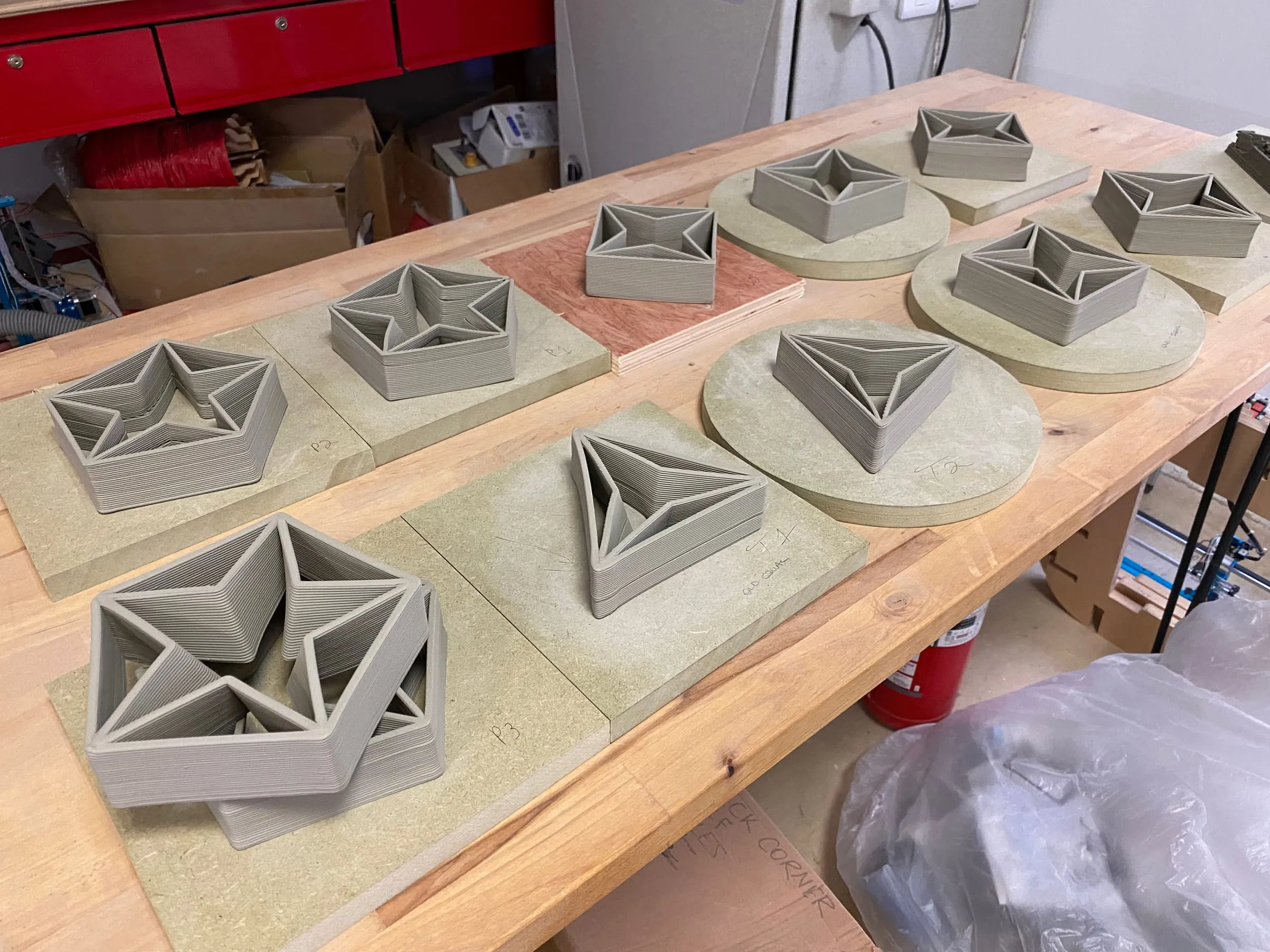 Freshly printed clay pieces with star and triangle cells, drying on boards on a workshop table